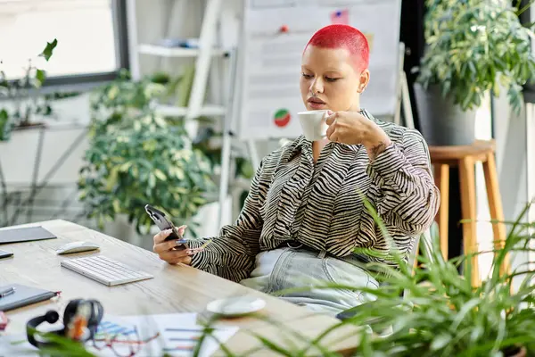 A confident bald woman with a red hairstyle enjoys coffee while using her phone in an office. — Stock Photo