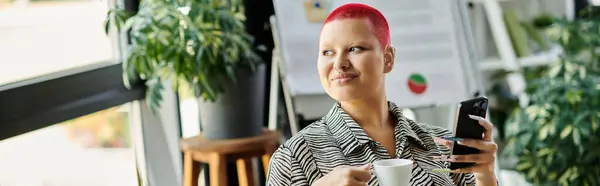 Uma bela mulher careca relaxa com uma xícara de café enquanto segura seu telefone em um escritório acolhedor. — Fotografia de Stock