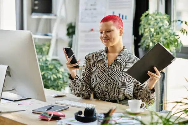 A confident bald woman holds a smartphone and a notebook, deeply engaged in work at her desk. — Stock Photo