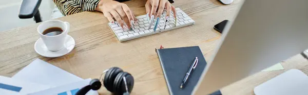 A dedicated individual types intently at her workspace, surrounded by notes and a warm drink. — Stock Photo