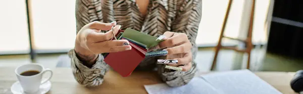 The beautiful bald woman examines vibrant fabric swatches as she sips her coffee in a bright space. — Stock Photo