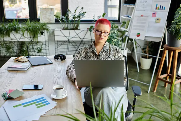 A stylish bald woman engages with her laptop in a vibrant office filled with plants. — Stock Photo