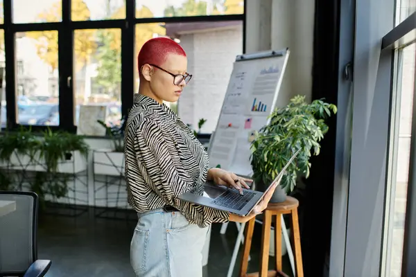 A focused individual engages with her laptop amidst a vibrant office atmosphere. — Stock Photo