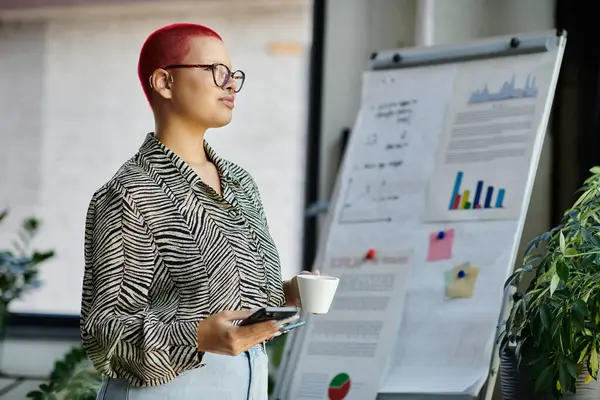 A woman with shaved hair and glasses engages in a work presentation while enjoying a cup of coffee. — Stock Photo