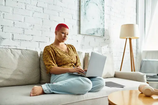 The bald woman focuses intently on her laptop while sitting comfortably on the sofa. — Stock Photo