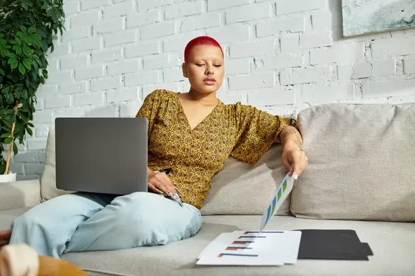 A bald woman with red hair thoughtfully examines colorful charts while working from home. — Stock Photo
