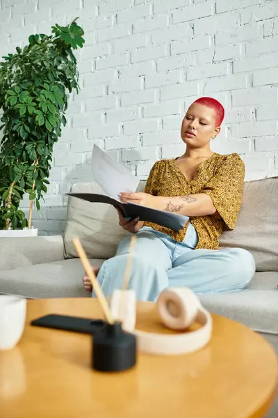 A beautiful bald woman relaxes on a couch, immersed in reading while surrounded by greenery. — Stock Photo