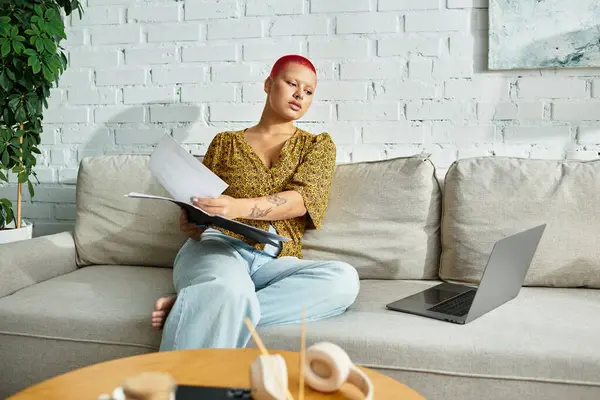 Una mujer calva con estilo se relaja en un sofá, revisando papeles importantes con enfoque. - foto de stock