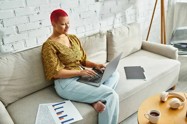 A bald woman engages in creative work, focused on her laptop in a cozy space. — Stock Photo