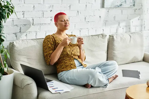 A bald woman savoring a warm cup of tea while relaxing on a comfortable sofa — Stock Photo