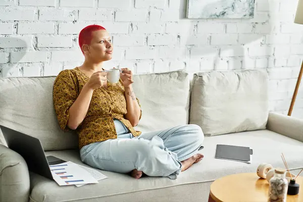 A bald woman savors her coffee while relaxing on a comfortable sofa in a chic living space. — Stock Photo
