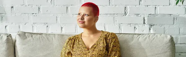 A striking bald woman with red hair poses gracefully on a cozy couch, lost in thought. — Stock Photo