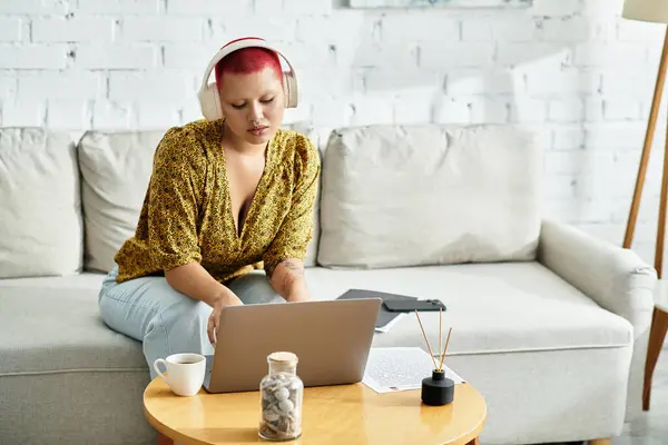 A stunning bald woman immersed in her work on a laptop while sitting on a comfortable couch. — Stock Photo