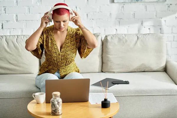 A bald woman calmly adjusts her headphones while focused on her laptop, surrounded by cozy decor. — Stock Photo