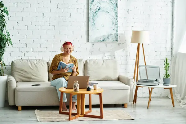 A woman with a radiant smile reads a book while sitting comfortably in her living room. — Stock Photo