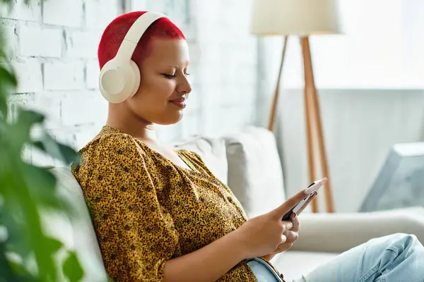 A bald woman relaxes on a couch while listening to music, fully immersed in her mobile device. — Stock Photo