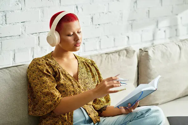 The bald woman wears headphones and thoughtfully engages with her book in a relaxed setting. — Stock Photo