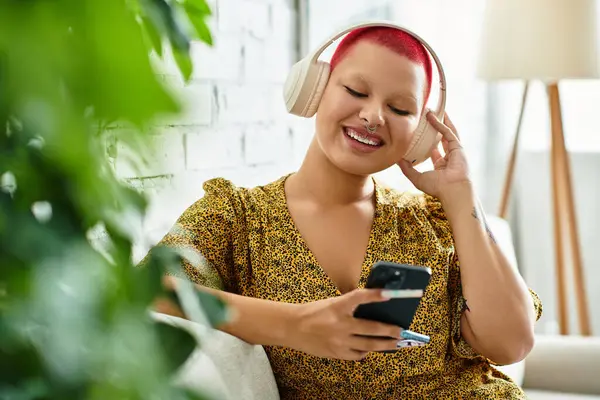 A cheerful bald woman listens to music, smiling while sitting comfortably in her cozy space. — Stock Photo