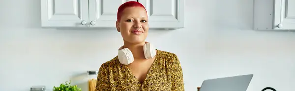 Une femme chauve aux cheveux vibrants se tient dans une cuisine charmante, rayonnant de confiance et de créativité. — Photo de stock