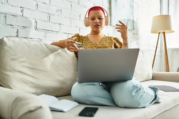 The bald woman with vibrant hair chats animatedly on a couch with her laptop. — Stock Photo