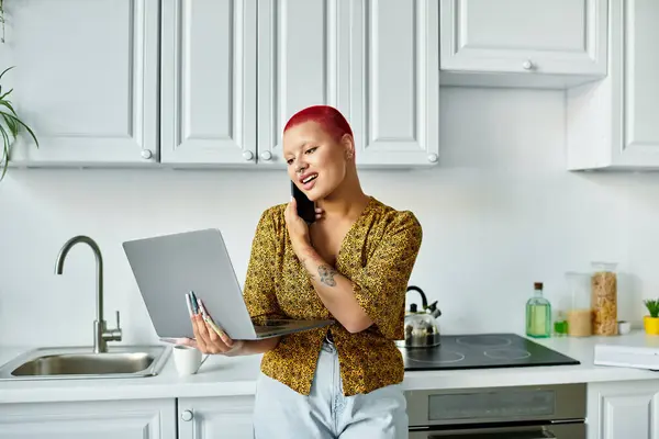 Uma mulher careca vibrante se envolve em uma conversa telefônica enquanto trabalha em seu laptop. — Fotografia de Stock