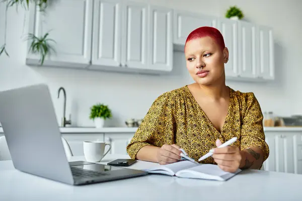A bald woman with vibrant red hair sits at a table, contemplating her thoughts while writing. — Stock Photo