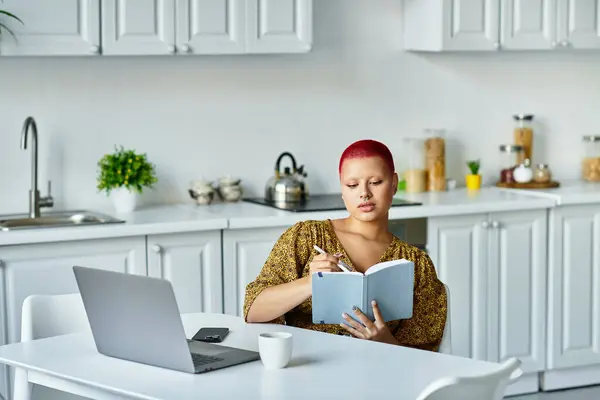 A bald woman writes in her journal at a sunny kitchen table, lost in thought. — Stock Photo