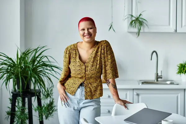 A joyful bald woman dressed in a stylish outfit stands gracefully by a kitchen table, smiling. — Stock Photo