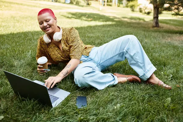 A bald woman with a cheerful smile enjoys her laptop while sipping coffee surrounded by nature. — Stock Photo