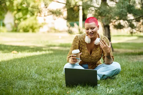 A cheerful bald woman relaxes in a park, sipping coffee and interacting with her laptop. — Stock Photo
