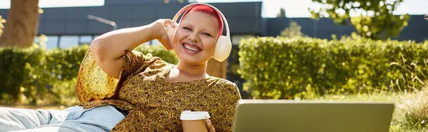 A cheerful bald woman listens to music, smiling broadly while lying on the grass. — Stock Photo