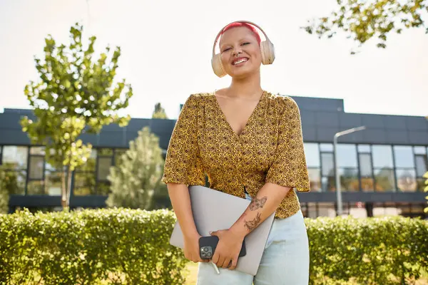 A bald woman with a warm smile holds her laptop under the bright sun, enjoying her workday outside. — Stock Photo