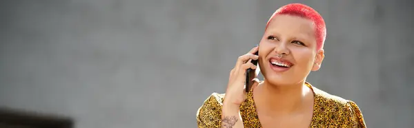 A joyful bald woman with pink hair enjoys a phone conversation in a stylish outfit. — Stock Photo