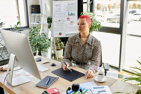 A bald woman with striking pink hair focuses on her tasks while seated at a modern desk. — Stock Photo