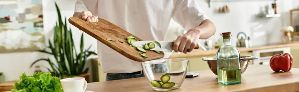 A handsome young man in a modern kitchen skillfully slices cucumbers for a vibrant homemade salad. — Stock Photo