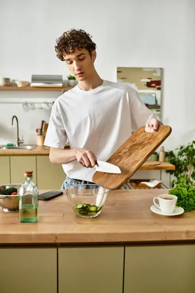 A young man with curly hair makes a fresh salad in a modern kitchen, embracing a healthy lifestyle. — Stock Photo