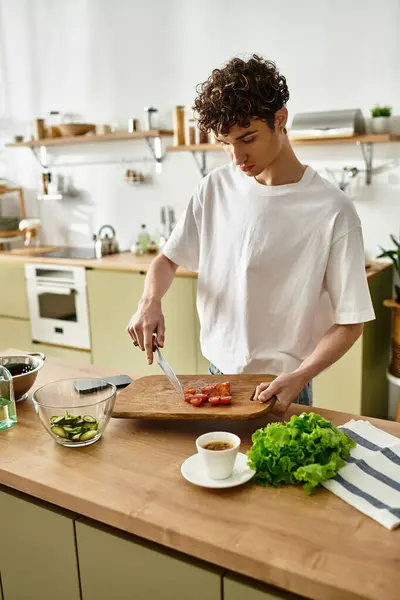 In einer eleganten Küche zaubert ein hübscher junger Mann mit lockigem Haar einen lebhaften Salat, der gesunde Gewohnheiten präsentiert. — Stockfoto