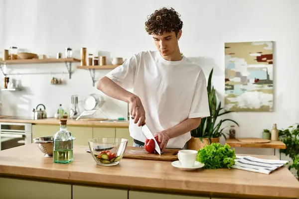 A stylish young man is chopping vegetables to create a vibrant salad while enjoying his time in a sleek kitchen. — Stock Photo