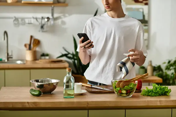 A handsome young man in a modern kitchen is making a fresh salad, embracing healthy eating habits. — Stock Photo
