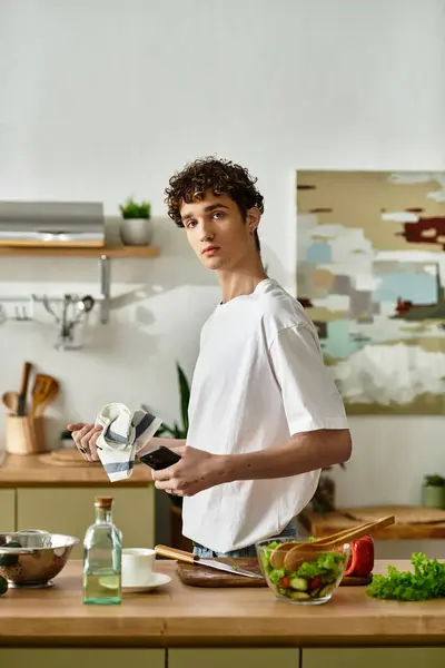 Ein gutaussehender junger Mann mit lockigem Haar bereitet in seiner modernen Küche gekonnt einen frischen Salat zu. — Stock Photo