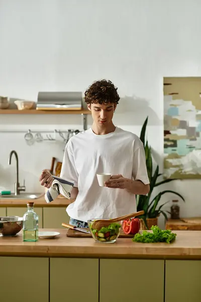 Ein junger Mann mit lockigem Haar trinkt Kaffee in der modernen Küche und pflegt einen gesunden Lebensstil. — Stockfoto