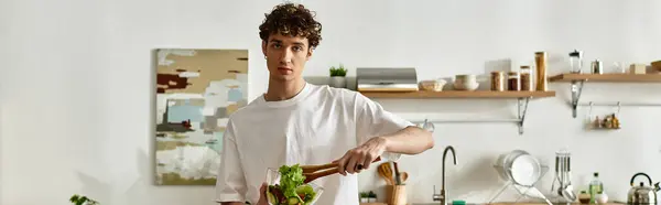 A handsome young man creates a salad, embodying healthy living in a sleek kitchen setting. — Stock Photo