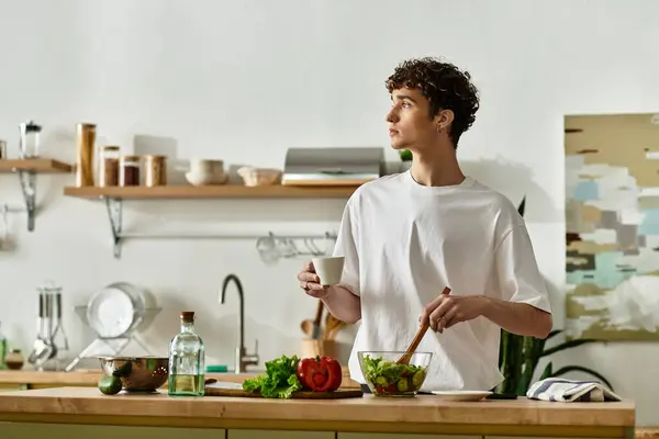 Ein junger Mann mit lockigem Haar mixt in einer stilvollen Küche einen lebhaften Salat und fördert so einen gesunden Lebensstil. — Stockfoto