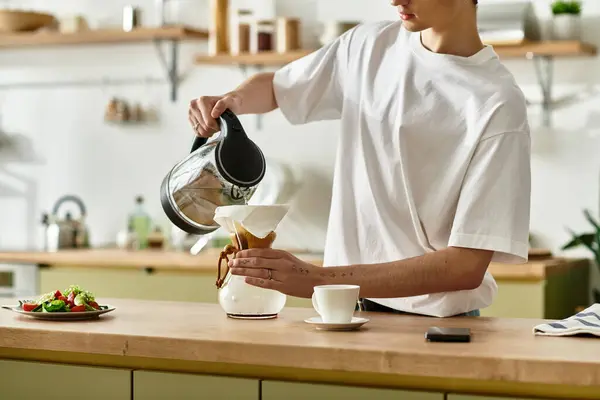 En medio de una cocina luminosa, un joven con el pelo rizado vierte café, saboreando el ambiente relajante de la tarde. - foto de stock