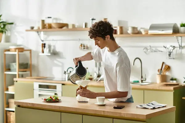 El joven vierte café humeante en una taza mientras prepara un delicioso desayuno en una cocina soleada. - foto de stock