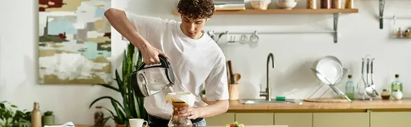 A handsome young man with curly hair expertly brews coffee in a cozy, sunlit kitchen filled with greenery. — Stock Photo