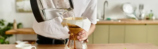 Um jovem prepara café fresco com cuidado em um espaço de cozinha brilhante e acolhedor. — Fotografia de Stock