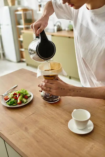 El joven vierte agua caliente en un filtro de café, saboreando un momento culinario en casa. - foto de stock
