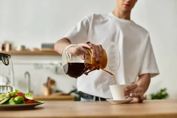 Un joven disfruta del momento mientras vierte café aromático en una taza limpia, mejorando su rutina matutina. - foto de stock