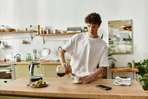 El apuesto joven vierte café recién hecho en una taza mientras saborea su desayuno en casa.. - foto de stock